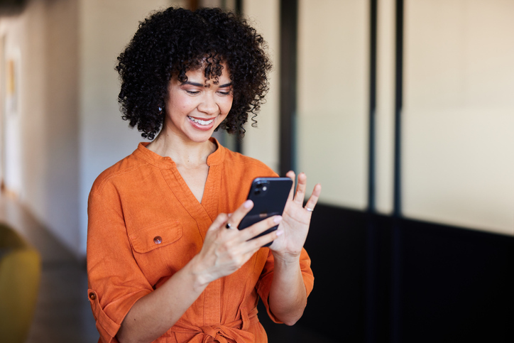 A smiling worker using a phone for a virtual care appointment, representing easy access to $0 urgent care, mental health, and primary care services.