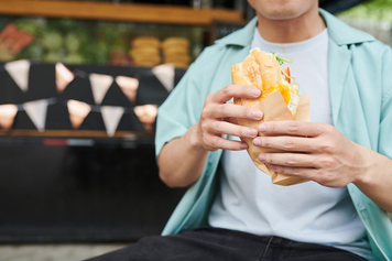 Close-up of young hungry man in casualwear holding appetizing hotdog stock photo